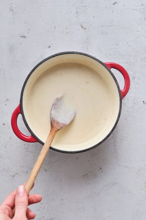 Creamy soup in a black and red pot with a wooden spoon, ready to serve.