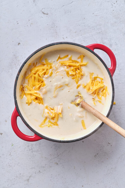 Creamy cheese sauce cooking in a red cast iron skillet with shredded cheddar cheese on top.