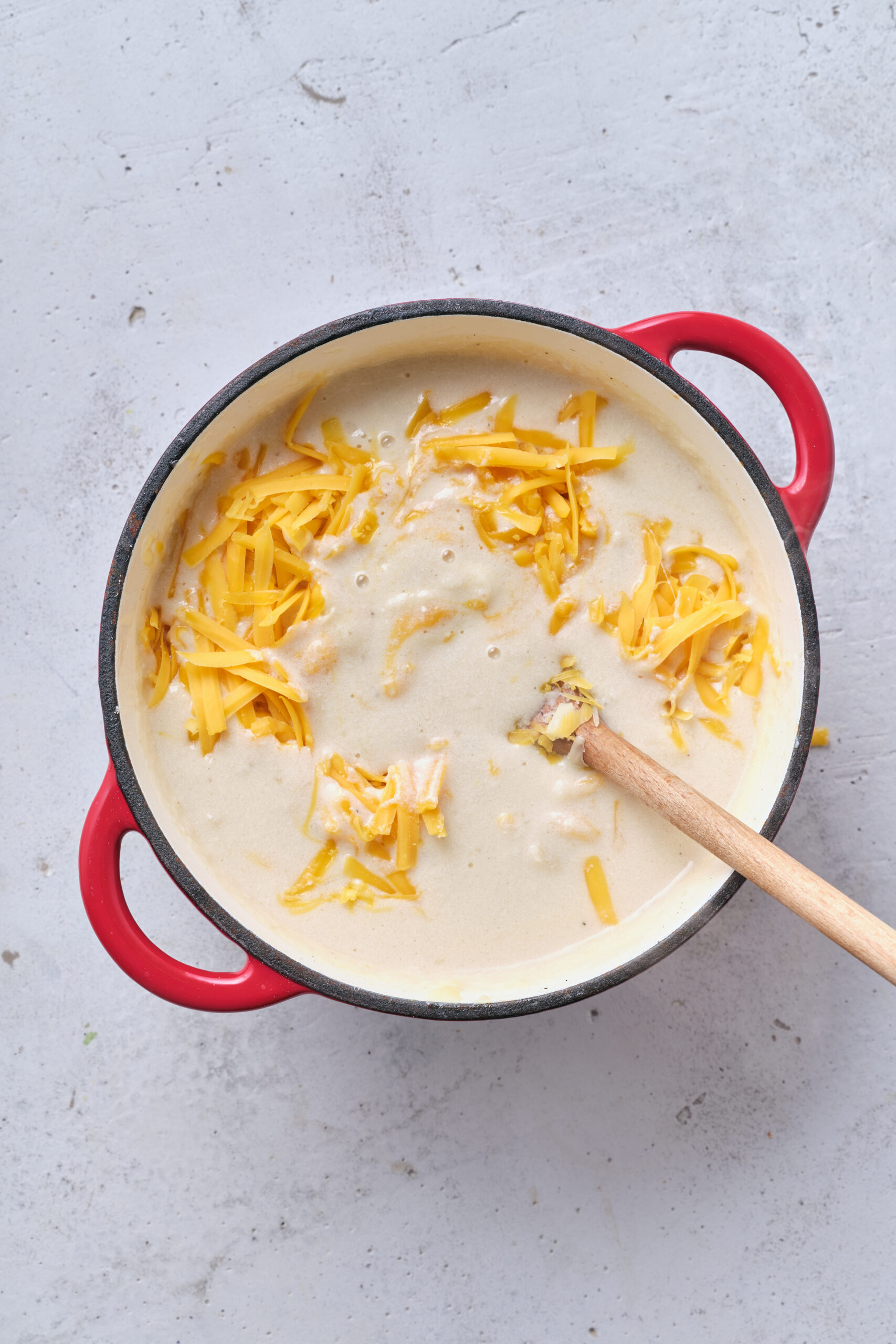 Creamy cheese sauce cooking in a red cast iron skillet with shredded cheddar cheese on top.