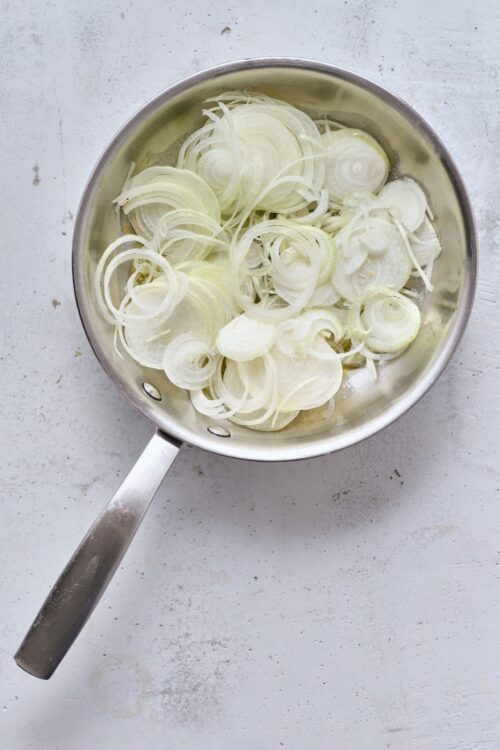Sliced onions in a stainless steel pan, ready for cooking or caramelizing. Perfect for savory recipes and flavorful dishes.