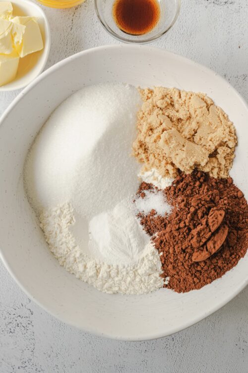 Butter, sugar, cocoa powder, flour, vanilla extract, and baking ingredients in a white bowl for baking recipes.