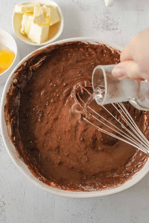 Rich chocolate cake batter being mixed in a large bowl with a whisk.