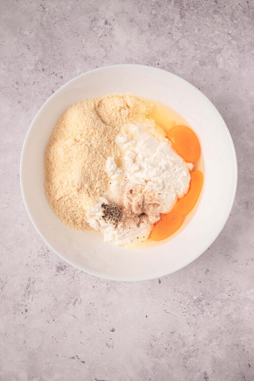 Flour, eggs, and seasoning in a white mixing bowl for baking or cooking ingredients.