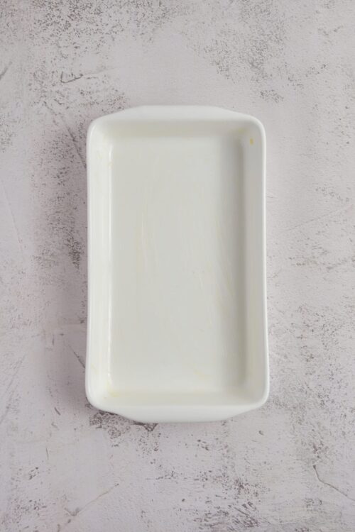 Uncovered white ceramic baking dish on textured light pink surface.