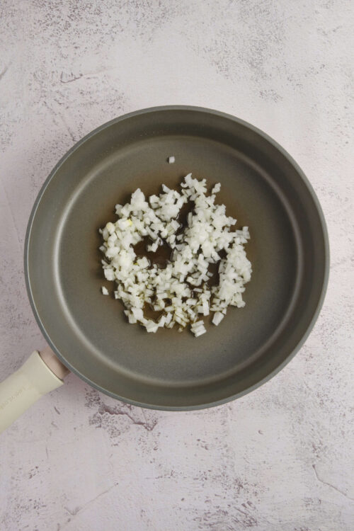 Diced onions cooking in a non-stick frying pan, preparing for a baked onion dish.