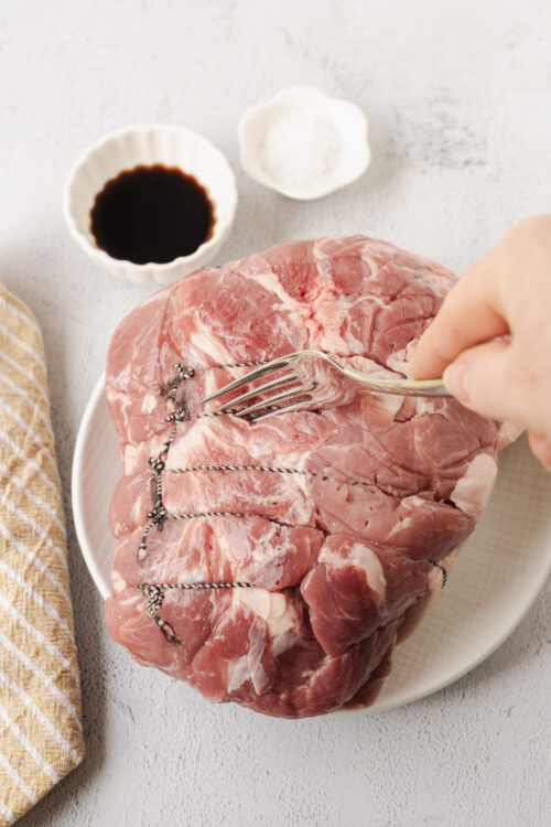 Raw pork shoulder with string being tied for roasting.