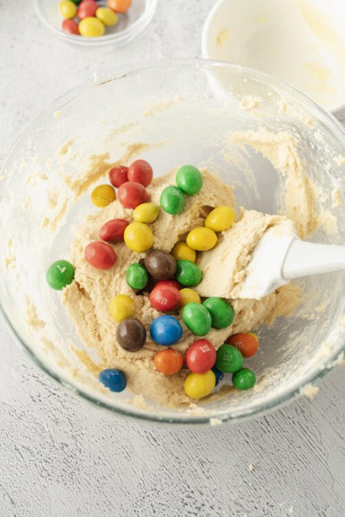 Colorful M&M cookie dough mixture in a glass bowl, ready for baking.