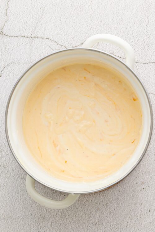 Creamy cheese sauce in a white enamel pot on a textured surface.