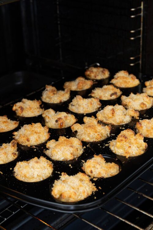Crispy baked chicken pot pie bites on a black baking sheet in the oven.