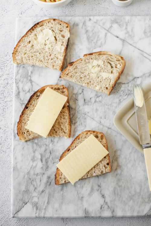 Soft artisan bread with butter and cheese slices on marble board.
