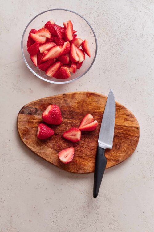 Fresh sliced strawberries in a glass bowl on a clean surface.