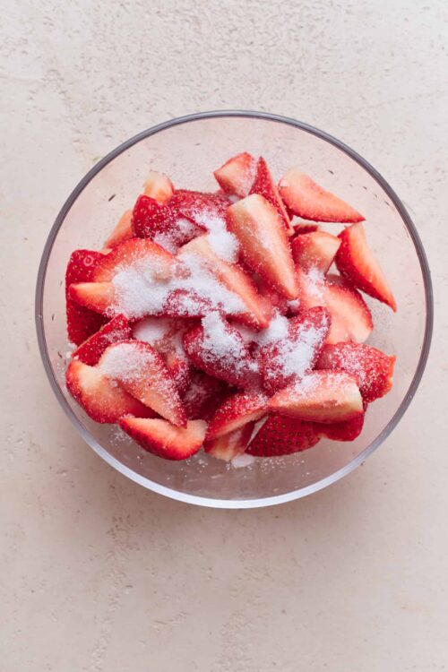 Fresh sliced strawberries sprinkled with sugar in a clear glass bowl.