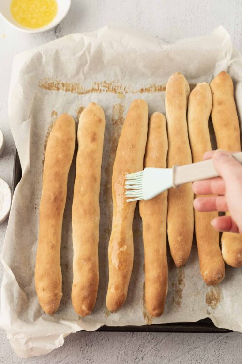 Golden baked breadsticks brushed with butter on parchment paper.