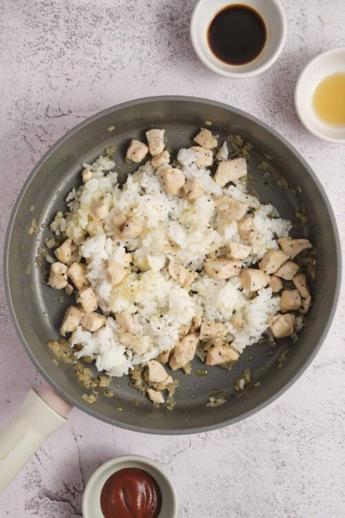 Sautéed chicken and rice in a skillet with soy sauce and seasonings.