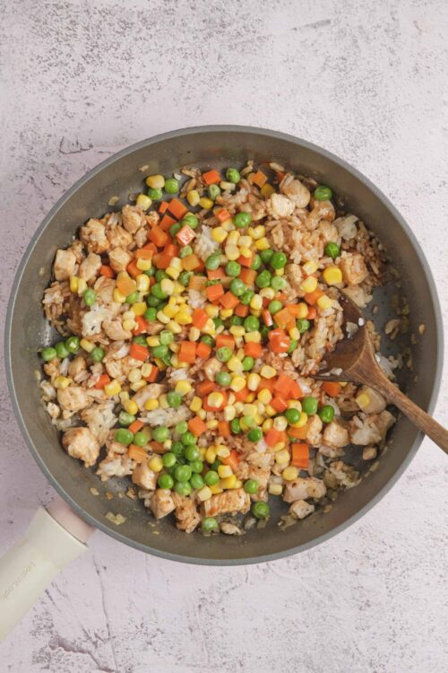 Colorful chicken fried rice with mixed vegetables in a frying pan.