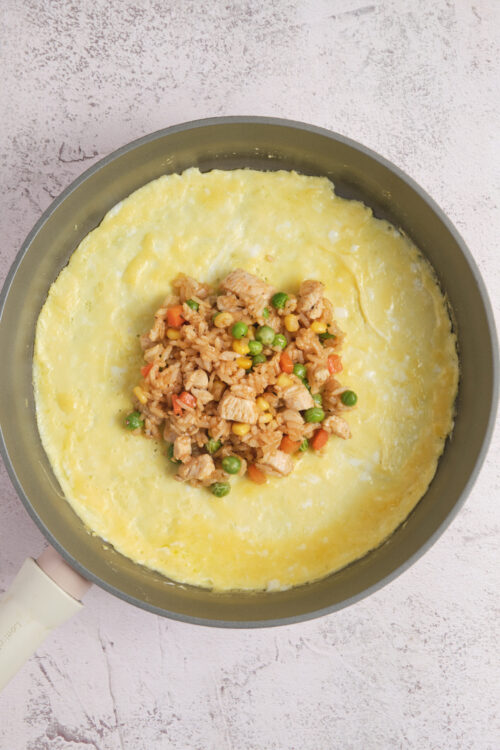 Scrambled eggs with chicken, vegetables, and rice in a skillet.