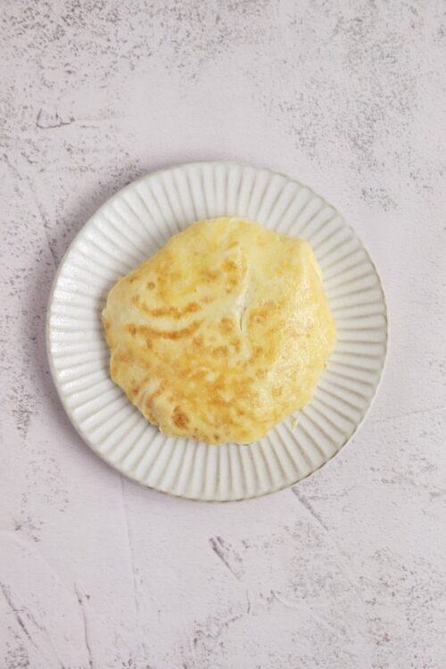 Fluffy cheesy baked biscuit on a white ruffled plate against a pastel textured background.