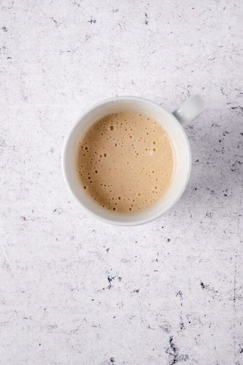 Creamy chai tea latte in a white mug on a textured white surface.