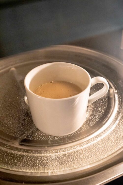 Steaming cup of freshly brewed coffee in a white mug inside a microwave oven.
