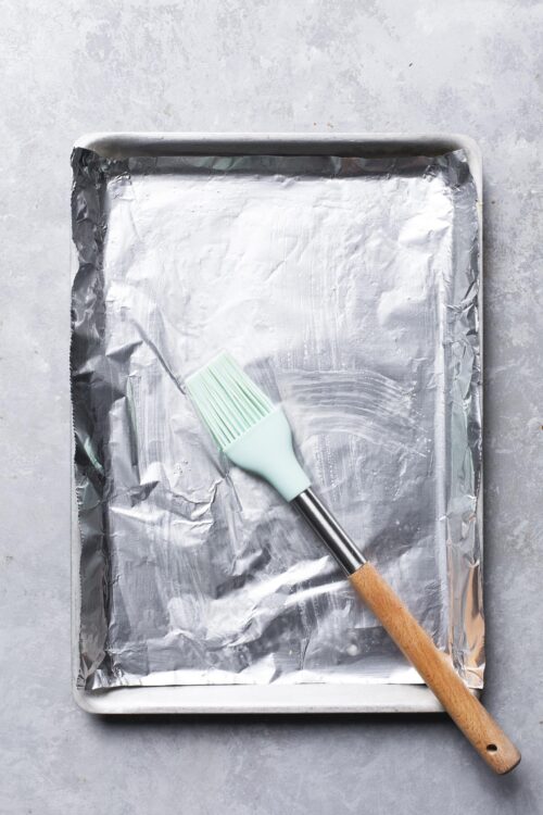 Aluminum baking sheet with parchment paper and silicone pastry brush for baking preparation.
