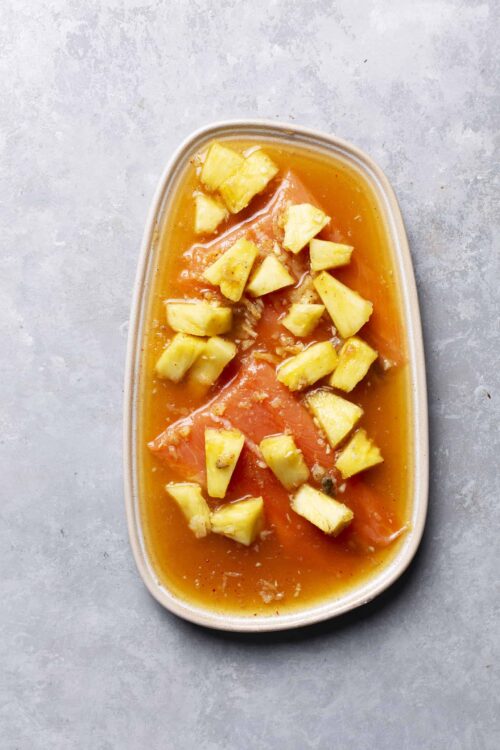 Golden pineapple chunks with fresh fruit compote in a beige dish for delicious dessert or snack.