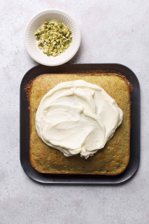 Cream cheese frosting on a freshly baked vanilla cake with chopped pistachios. Perfect for cakes, dessert recipes, and special occasions.