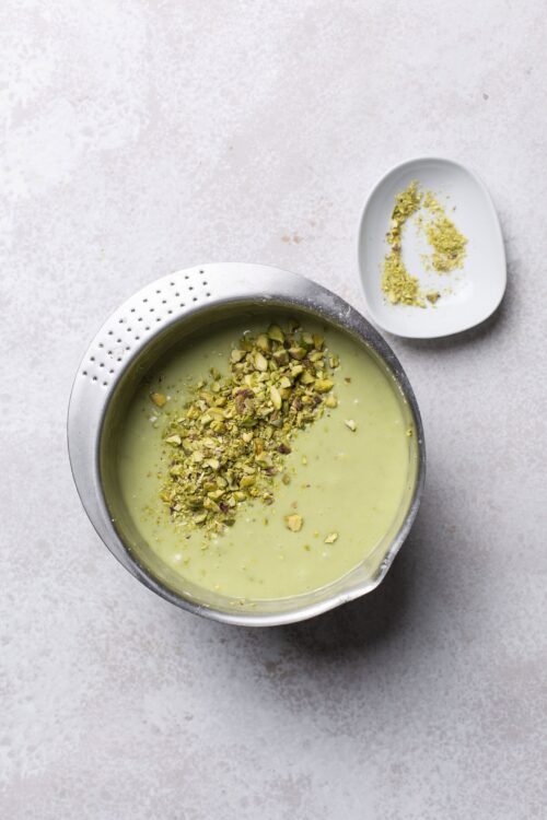 Sweet pistachio custard dessert topped with chopped pistachios, served in a metal bowl.