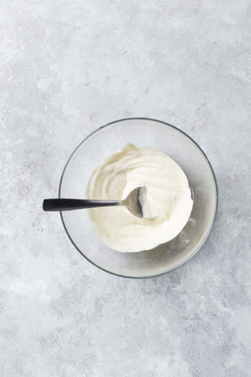 Creamy homemade mayonnaise in a glass bowl with a spoon.