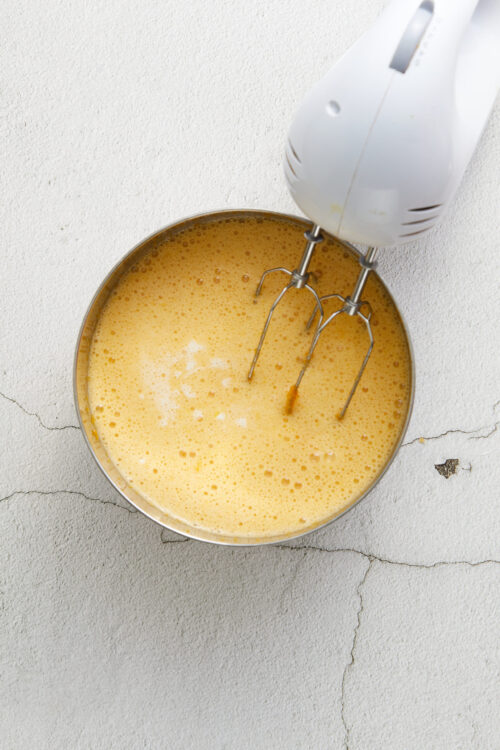 Fluffy beaten eggs in mixing bowl with hand mixer, preparing for baking or cooking.
