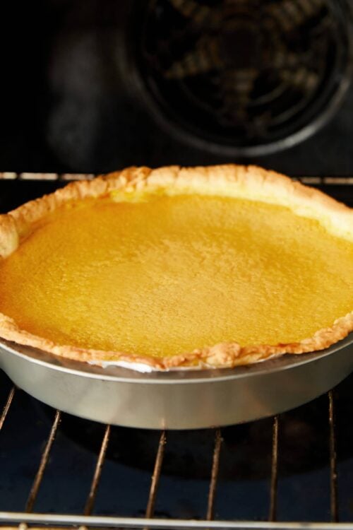 Creamy lemon tart baking in oven on a wire rack, golden crust and smooth lemon filling.