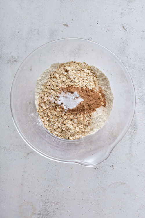 Oatmeal, cinnamon, sugar, flour, baking ingredients in glass mixing bowl for healthy baking.