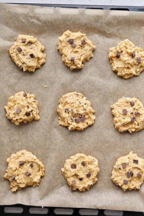 Creamy chocolate chip cookie dough scoops on baking sheet, ready to bake.