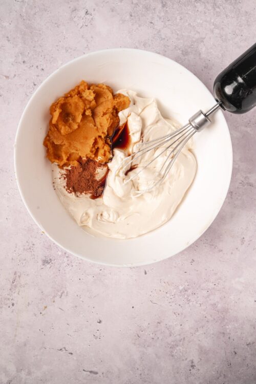 Cream cheese frosting with brown sugar, pumpkin puree, and vanilla extract in a bowl ready for mixing.