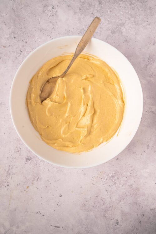 Creamy vanilla frosting in a white bowl with a metal spoon, perfect for baked goods and cakes.