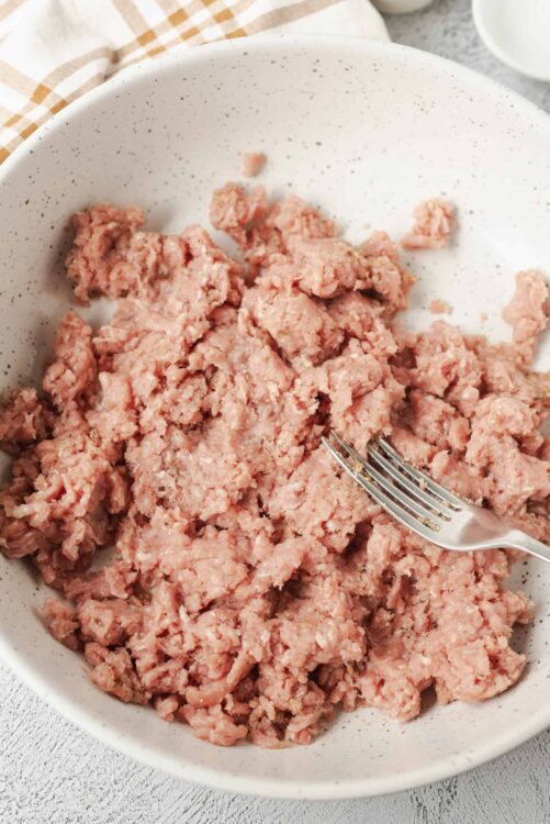 Ground raw meat in a white speckled bowl with a metal fork for baking and cooking recipes.