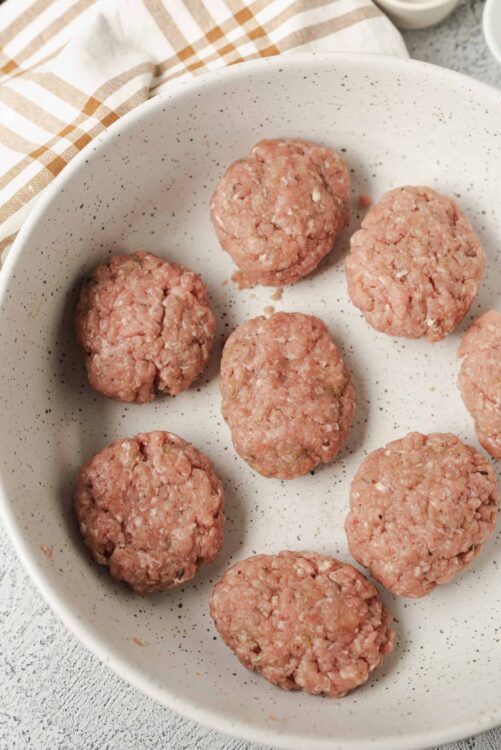 Seasoned raw meatballs in a white speckled baking dish for baking or cooking.