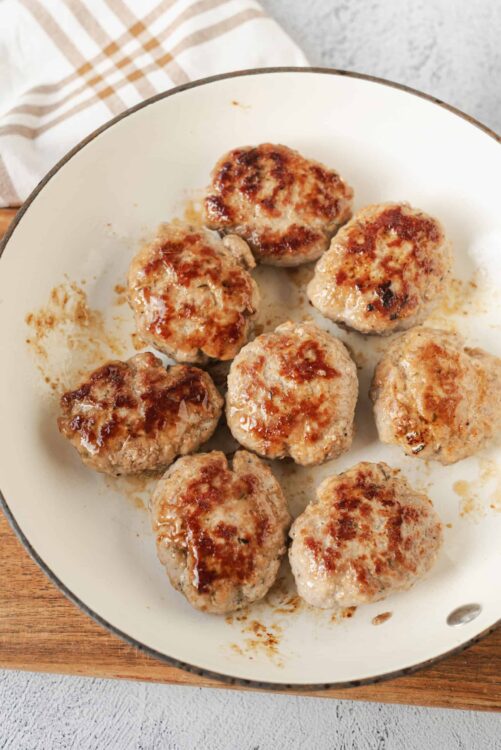 Juicy homemade meatballs cooking in a skillet on a wooden board.