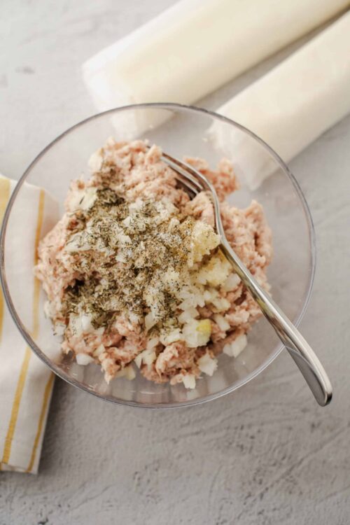 Seasoned ground chicken mixture with herbs and onions in glass mixing bowl.