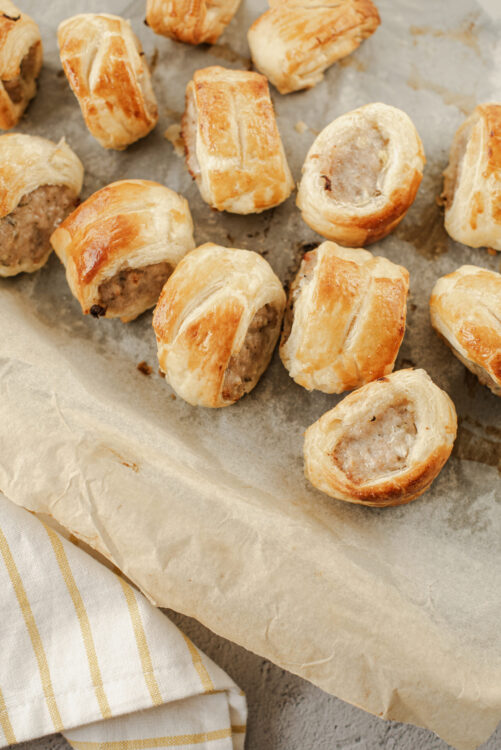 Golden baked sausage stuffed puff pastry bites on parchment paper.
