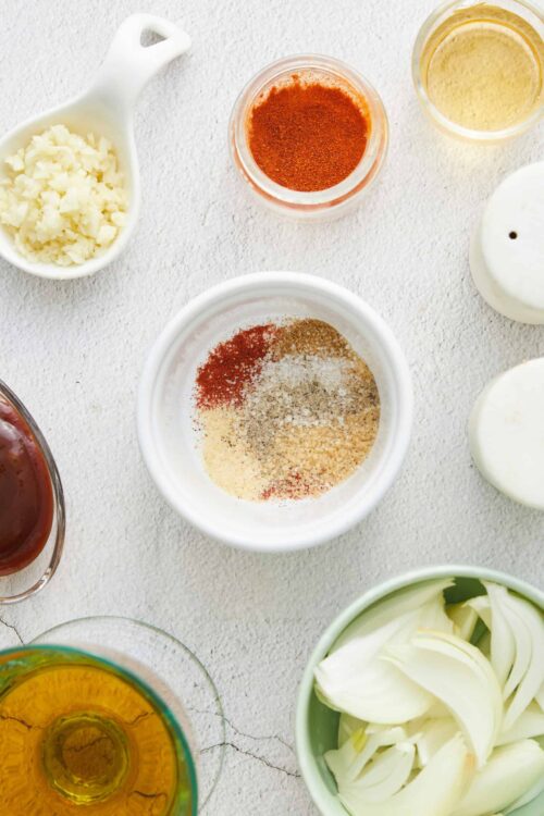Diced garlic, spices, and liquids for flavorful cooking, arranged on a white textured surface.