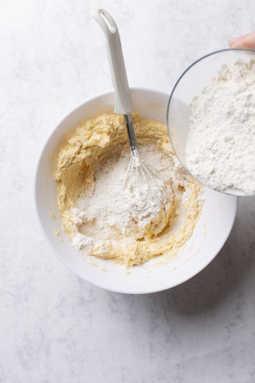 Flour being added to creamed butter and sugar in a mixing bowl for baking.