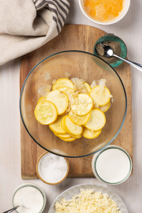 Sliced yellow summer squash and onions in a glass bowl for baking or cooking recipes.