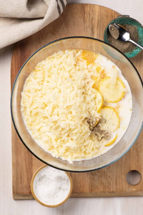 Creamy potato casserole ingredients with shredded cheese, lemon slices, and seasonings.