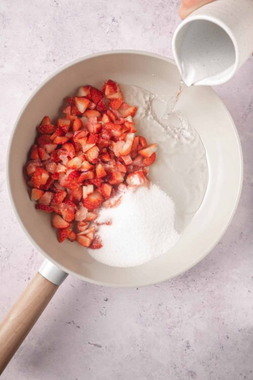 Fresh strawberries being combined with sugar and cream for a delicious dessert.