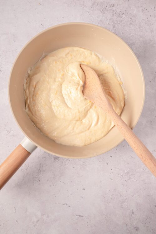 Creamy batter mixture in a beige mixing bowl with a wooden spoon on a light surface.