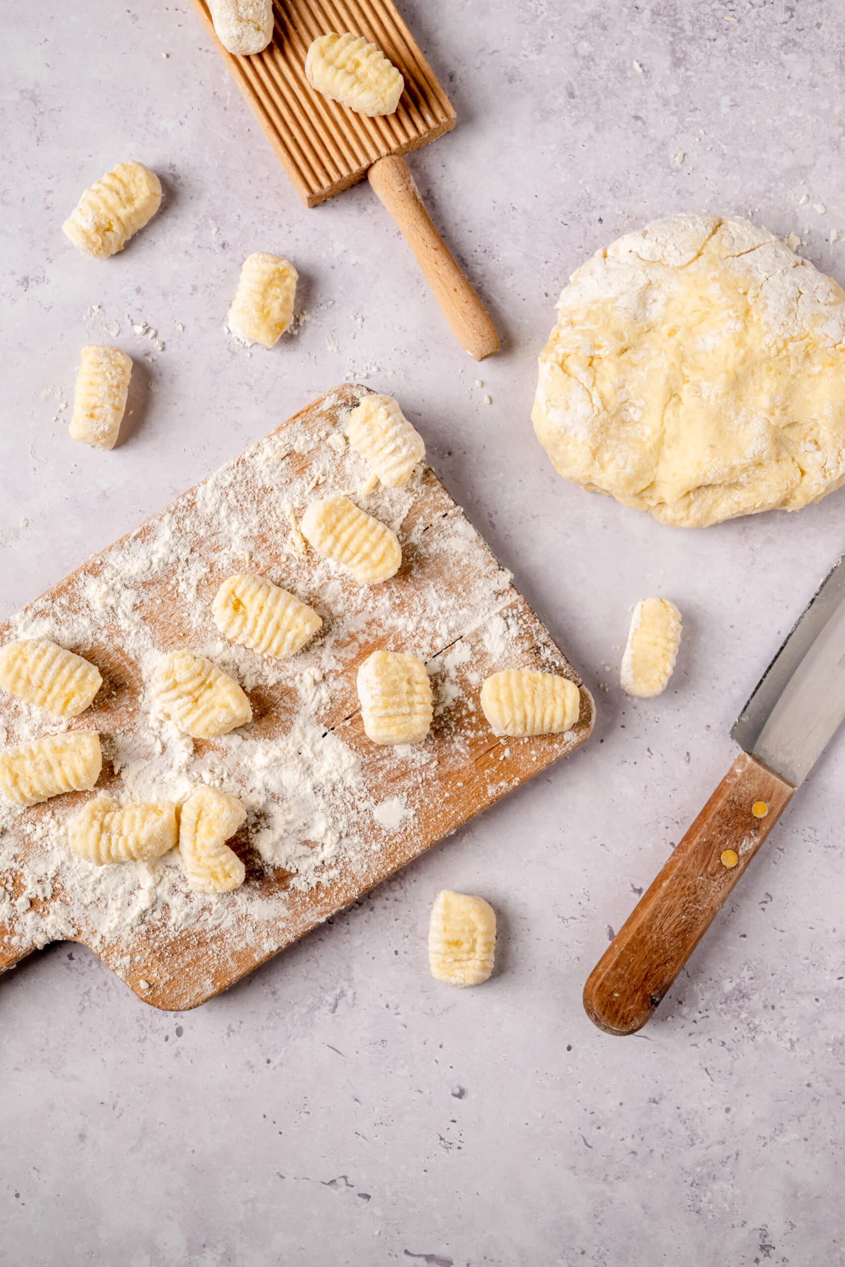 Homemade potato gnocchi dough with ridged gnocchi ready for cooking on a wooden cutting board.