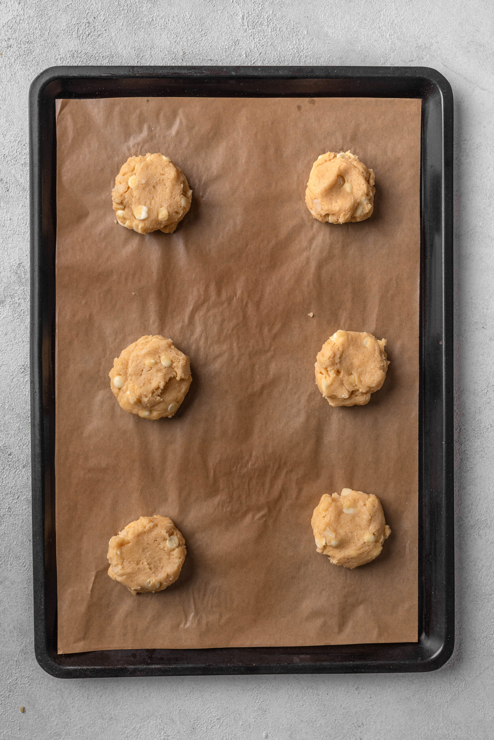 Soft white chocolate macadamia nut cookie dough balls on baking sheet.