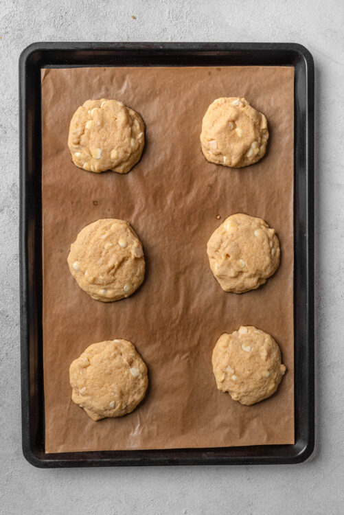 Butter cookies with white chocolate chips on baking sheet in oven-safe pan.