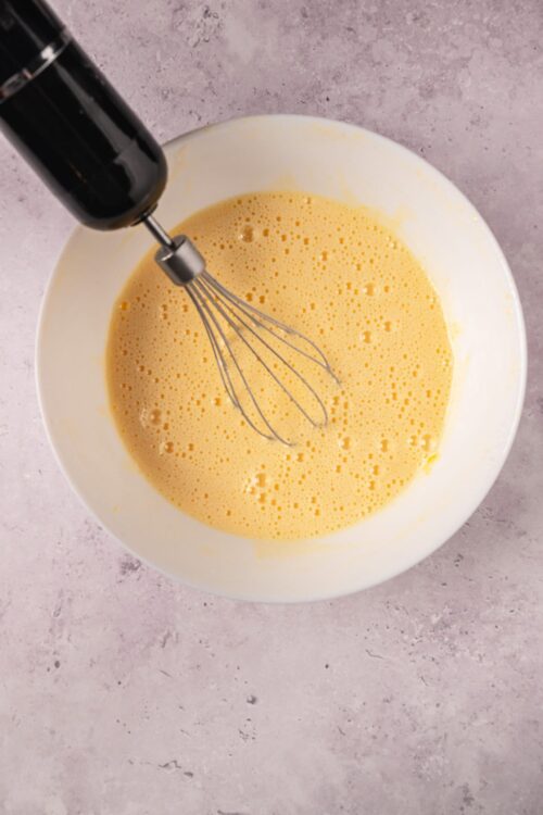 Fluffy yellow cake batter in a mixing bowl with a whisk and electric hand beater.