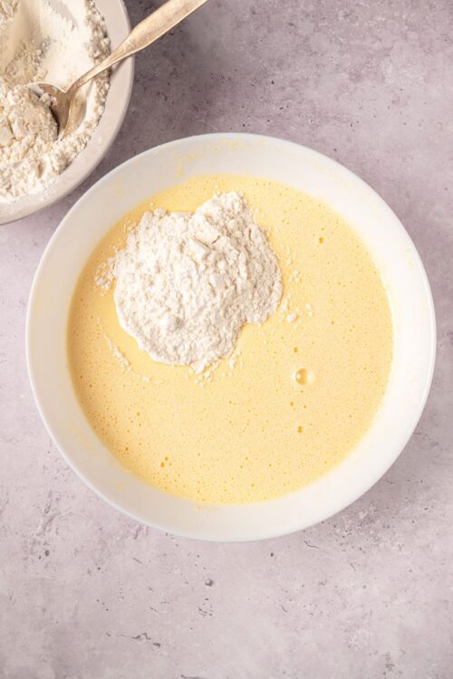Creamy batter with flour mixture in a white bowl for baking cake.